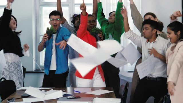 Group of creative crazy young diverse people students office workers colleagues throwing papers away in air, singing karaoke, dancing, having party. Freedom from work. Weekend chill out, days off