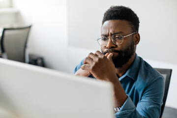 Thoughtful black man in eyeglasses stack with hard task, looking at computer screen, thinking of...