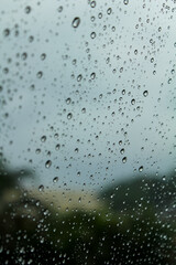 Close-up of the raindrops on car window, and blurred trees are in the background.