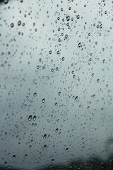 Close-up of the raindrops on car window with the grey sky as the background.