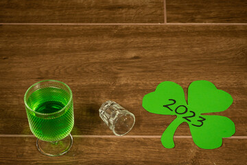 shot glass and goblet on wooden bar background filled with green spirit beer and shamrock, drunk at...