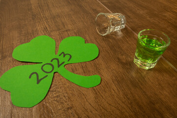 shot glass on wooden bar background filled with green spirit beer and shamrock, drunk at...