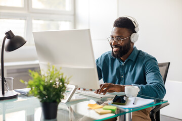 Happy black businessman in headset working on computer, making conference video call, sitting in...