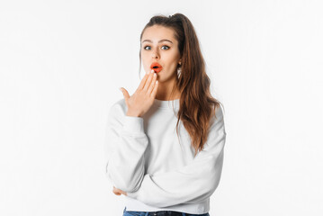 Ouch. Amazed young woman showing Oops expression at the camera. Portrait of young girl with long hair, arm cover mouth, standing against white studio background