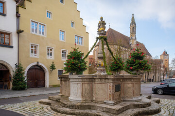 Fototapeta na wymiar Herrnbrunnen (Nobles Fountain) and Franciscan Church (Franziskanerkirche) at Herrngasse (Nobles Lane Street) - Rothenburg ob der Tauber, Bavaria, Germany