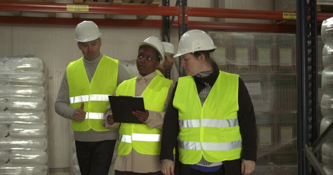 4k slow-motion video of the warehouse manager talking to workers and assigning new tasks while they are walking through storage compartments. One coworker is carrying the cardboard box and passing beh