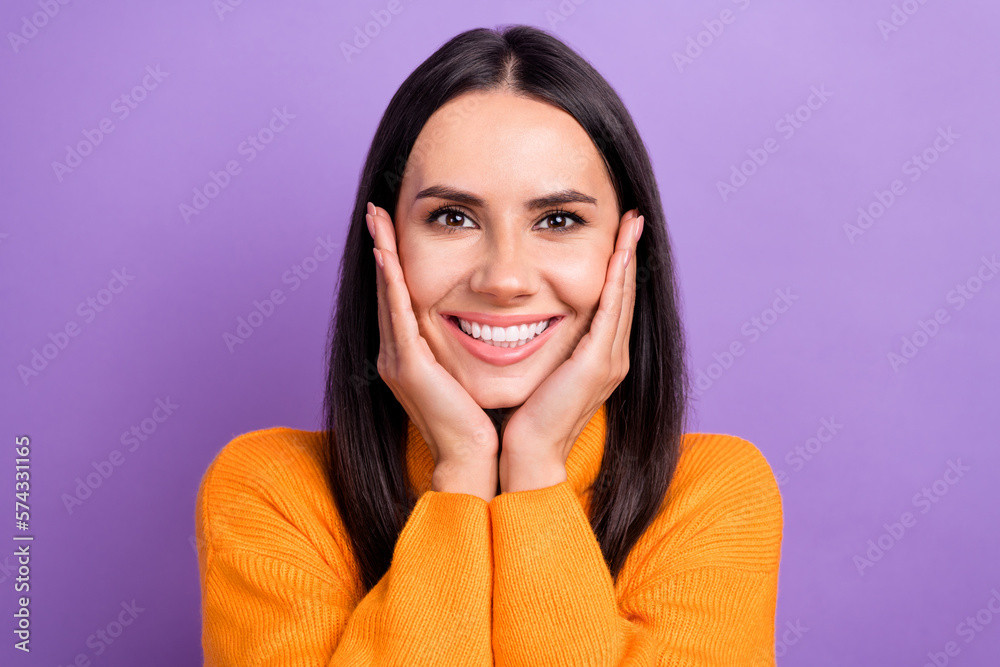 Wall mural Portrait photo of young cheerful gorgeous woman brunette hair wear orange stylish pullover touch cheeks beauty isolated on purple color background