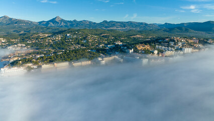 Fototapeta na wymiar Aerial view, flight above the clouds, the coast of Mallorca in the fog with the town of Santa Ponca, Mallorca, Spain