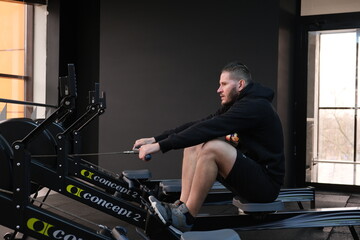  February 21, 2023 Ukraine, Dnipro. Rowing machine firm Concept 2. A man on a workout in the gym with his own weight. aeromagnetic simulator. Scandinavian traction for strength work of the back muscle © Neuro architect