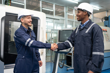 Two male engineer shaking hands after work success at factory. Smiling technician wearing uniform...
