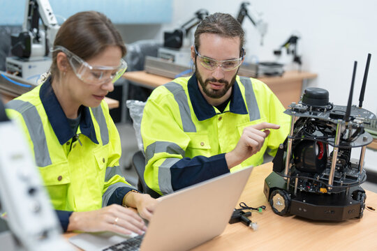 Male and female engineers using laptop computer coding program for control AI robot model in academy robotics automation laboratory room for using in manufacturing or industry
