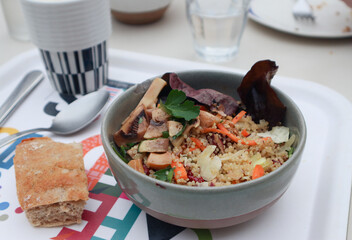 A bowl of healthy quinoa salad with mixed vegetables such as carrots, mushroom, red leaf lettuce, green parsley and walnuts with bread in a plate and spoon 