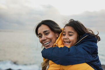 Happy latin mother and daughter having fun on the beach during winter time - Mom and child outdoor