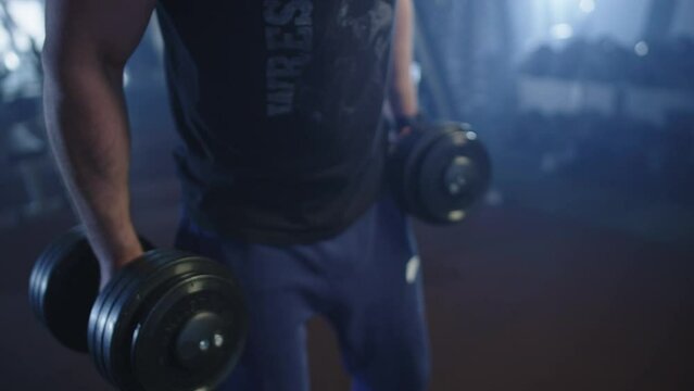 Caucasian man working out in the gym with dumbbells. An athlete pumps up his muscular arms while lifting a heavy weight. Workout and fitness is a healthy lifestyle.