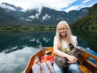 Woman with a french bulldog on her lap sitting in a row boat on a lake