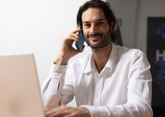 portrait d'un jeune homme souriant, employé de bureau assis devant son ordinateur au bureau. Il...
