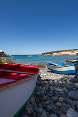 Cheap boats on a pebble beach. Red and white boat on the left, blue and white boat on the right. Bay of turquoise waters and brown and yellow hills in the background. La Caleta, Tenerife, Canary Islan