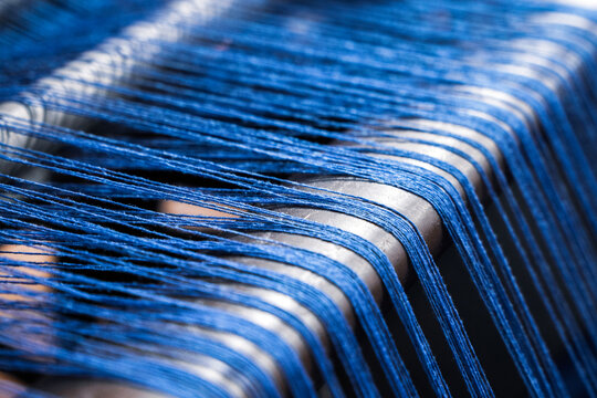 A close up of weaving machine. A loom machine for clothing or woven label. Weaving machine for garment industry. Yarn thread lines on the weaving loom machine for clothing in textile factory.