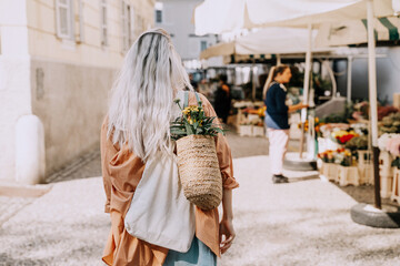 Beautiful young woman buying fresh flowers at city center market. Flower and food local market. Concept shopping, small business, sustainable production.
