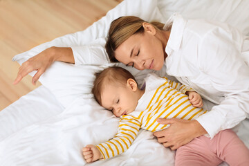 Fototapeta na wymiar Mother and little baby infant girl lying sleeping together in cozy white bed at home, above view, free space