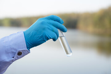 Closeup researcher hands wears blue gloves holds test glass tube that contain sample water from the...