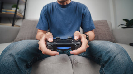 Excited young handsome man holding joystick controller playing video game sitting on the couch at home