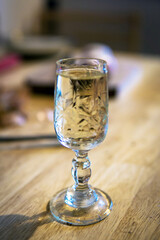 One glass filled with rakija standing on wooden table in the kitchen. Authentic hungarian palinka made from plum. Crystal glass, filled with traditional liquor. Blurred background.