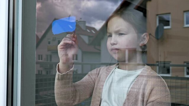 Little girl draws the flag of Ukraine on the window.