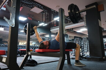 Fototapeta 
February 21, 2023 Ukraine, Dnipro.
Barbell bench press. A young athlete on a simulator in a supine position loads the muscles of his arms and chest. Training of muscle groups of the upper body. gym obraz