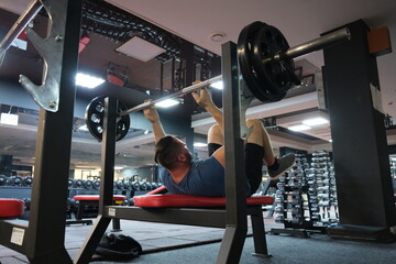
February 21, 2023 Ukraine, Dnipro.
Barbell bench press. A young athlete on a simulator in a supine...