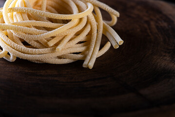 Uncooked traditional hand - rolled durum wheat pasta Pici of Tuscany, wooden rustic background and flour in studio light, macro photo of pasta pici and selective focus