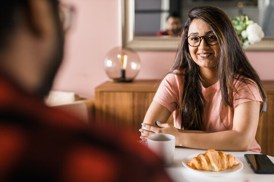 Young diverse loving couple eating croissant and talks together at home in breakfast time. Communication and relationship concept