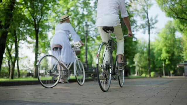 Cute mature couple riding bikes in city park, active seniors enjoying hobby