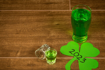 shot and pint glasses on wooden bar background filled with green spirit cocktail and shamrock,...