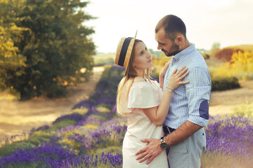 A couple in love in a field of lavender at sunset in good weather. Beautiful woman in a dress and straw panama with a man on the background of nature, love and feelings. Blue, purple lavender.