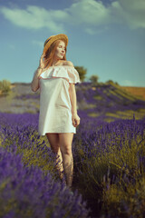 Fototapeta na wymiar Beautiful girl on the lavender field. Beautiful woman in the lavender field on sunset. Soft focus. Provence, France. A girl in pink dress and hat walking trough lavender fields and enjoys nature.