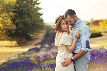 Fototapeta premium A couple in love in a field of lavender at sunset in good weather. Beautiful woman in a dress and straw panama with a man on the background of nature, love and feelings. Blue, purple lavender.