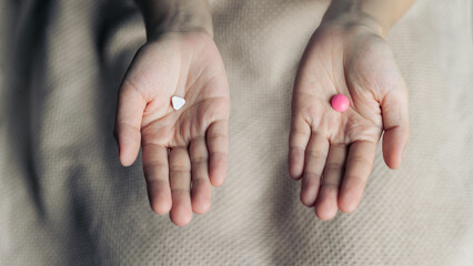 Female hands hold and offer two choice medicine pills capsule for chosen. White and pink candy or meds compare to choose from. Concept decision making or indecisiveness. - obrazy, fototapety, plakaty