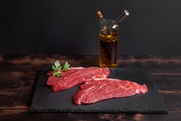 Raw minute steak of marbled beef on slate board, bottle with vegetable oil and balsamic vinegar