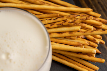 Thin and long bread sticks made of wheat flour and a glass of milk