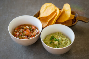 Homemade pico de gallo salsa and guacamole dip with chips on simple grey background