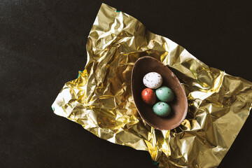 Easter chocolate eggs in metallic shiny gold paper paper on black background