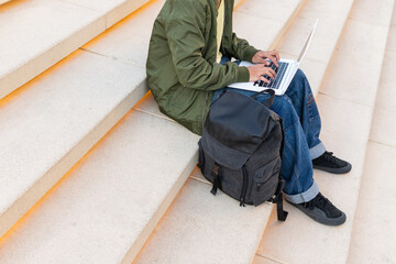 Anonymous student with backpack using laptop on stairs