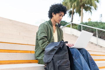 Focused ethnic student with backpack using laptop on stairs