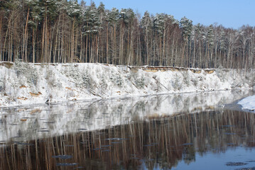 snow-covered trees in a nature park on the bank of a river where pieces of ice float in the water
