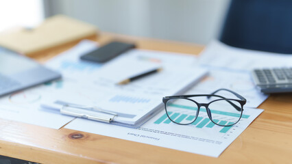 Desk of bookkeeper with balance sheet and calculator on desk, focused on eyeglass, nobody.