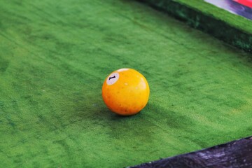 An orange billiard ball number one lies on a green stage on a billiard table 
