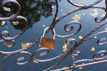 Forged metal in the form of various patterns and a hanging old door lock against the background of water in autumn. Abstract background. Closeup. Selective focus.