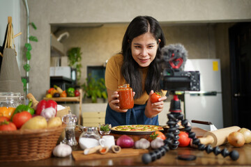 Beautiful happy Asian female chef baking a homemade pizza and making a cooking video live steaming on social media. 