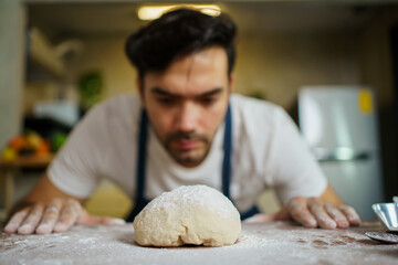 Happy cheerful Italian chef making a fresh pizza dough on wooden table in kitchen.